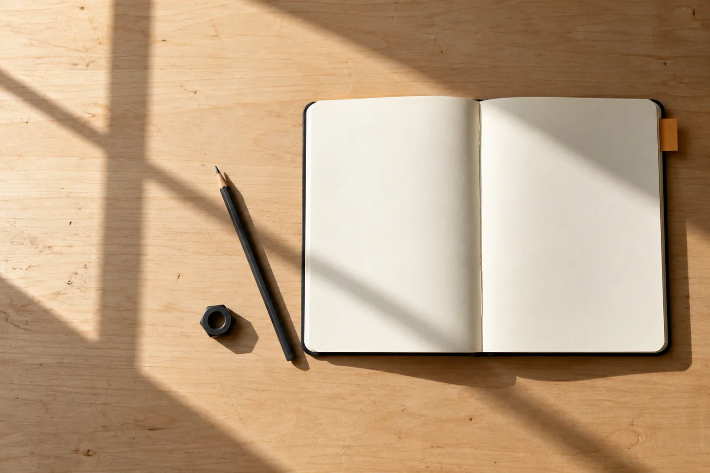 Blank notebook, pencil and fastener beneath a window shadow