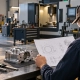 Estimator reviewing an engineering drawing and machined component at a machine shop